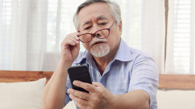 An old man struggles to see clearly at his phone.